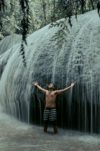 A man dressed in a black shorts stood before the waterfall
